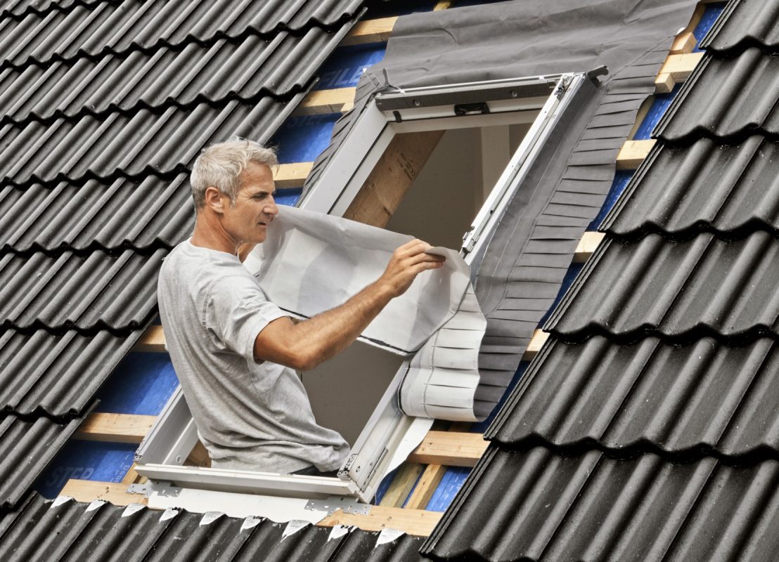 Ein Handwerker befestigt eine Anschlussschürze um den Blendrahmen eines Dachfensters herum.
