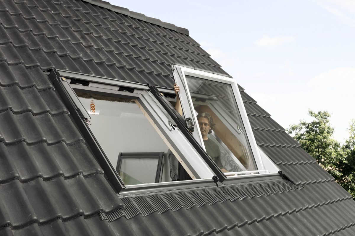 Ein Fensterprofi ist dabei, ein Dachfenster auszutauschen. Links daneben befindet sich ein noch leerer Dachfensterrahmen.