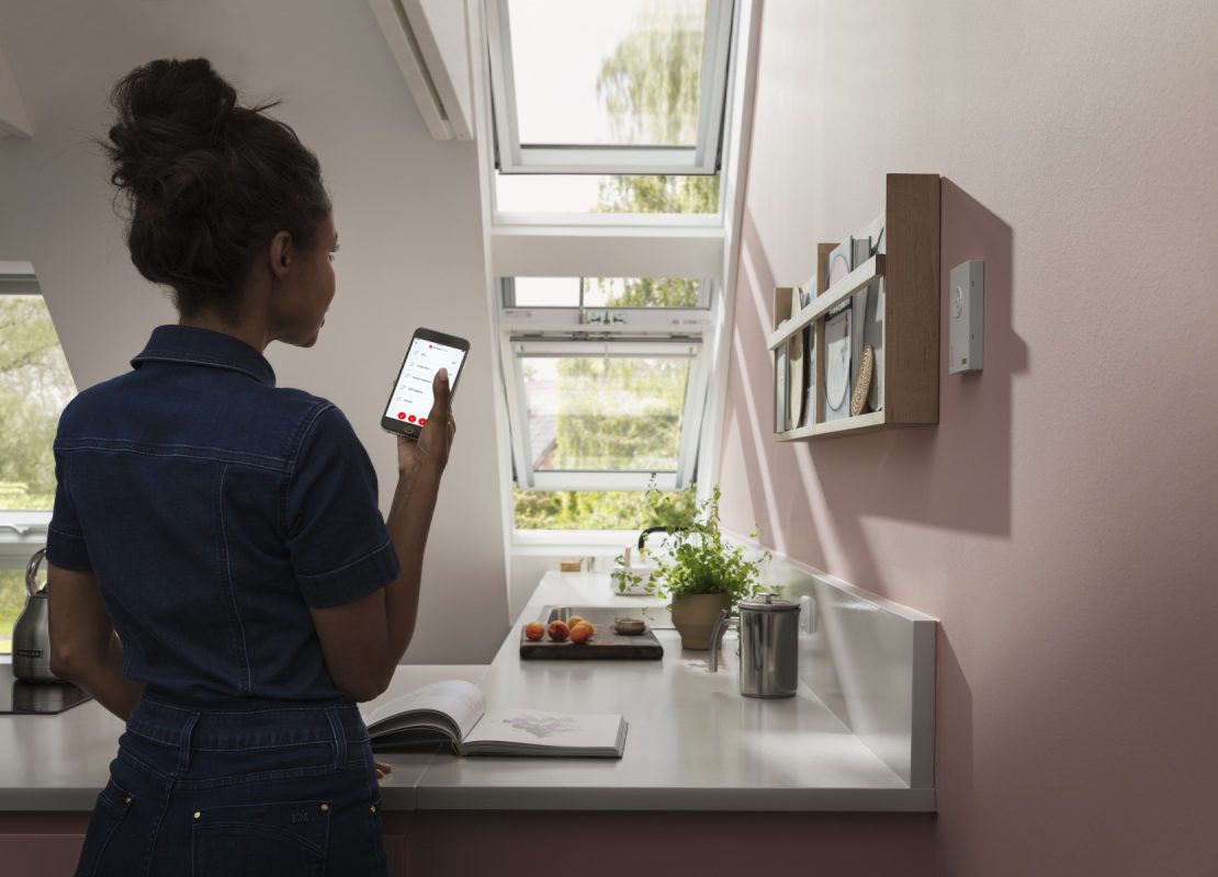 Eine junge Frau steuert nach dessen Einbau ihr Dachfenster per App.